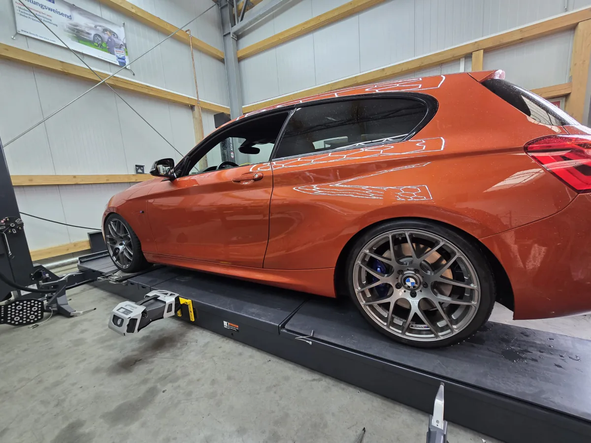Messkopf am Vorderrad eines orangen BMW 1er während der 3D-Achsvermessung