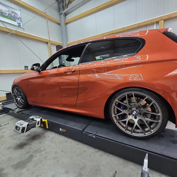 Messkopf am Vorderrad eines orangen BMW 1er während der 3D-Achsvermessung